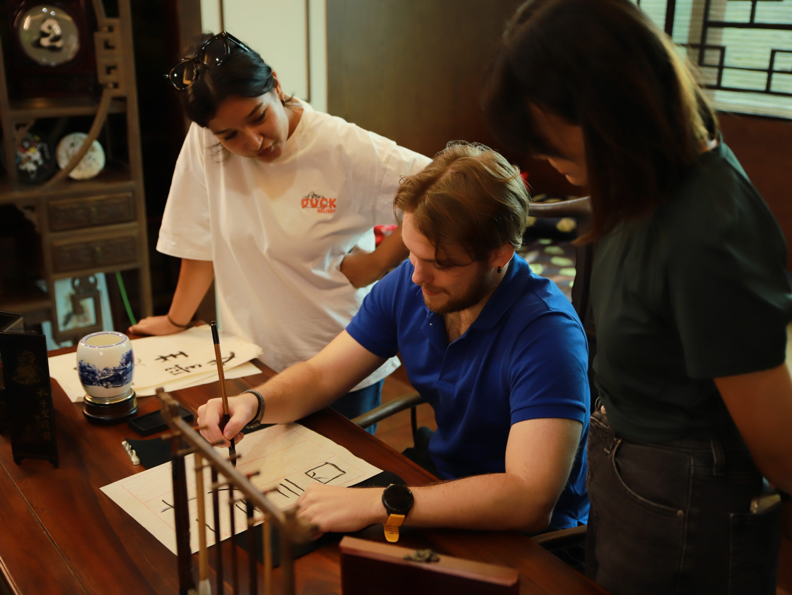 Three international students practicing traditional Chinese calligraphy with a brush and ink during their study in Taiwan at I-Shou University.